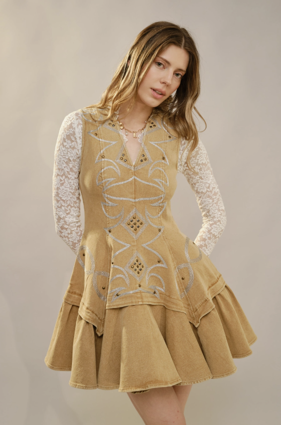 Woman wearing a beige embroidered dress with a white lace top against a plain background