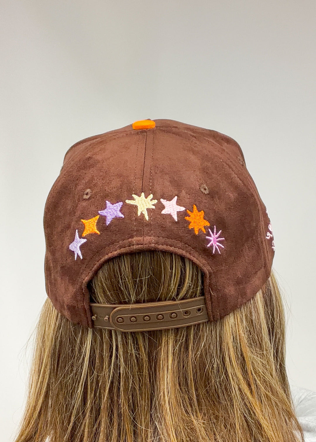 Woman wearing brown faux suede hat with stars embroidered across back on plain background