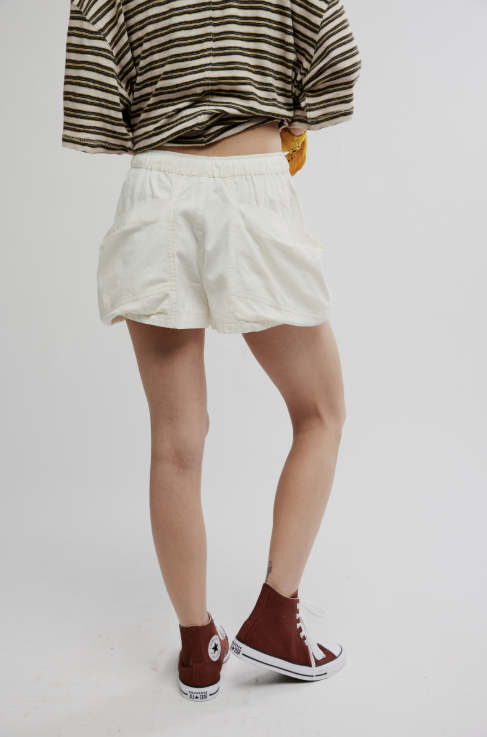 Person wearing white shorts and brown high-top sneakers on a plain background