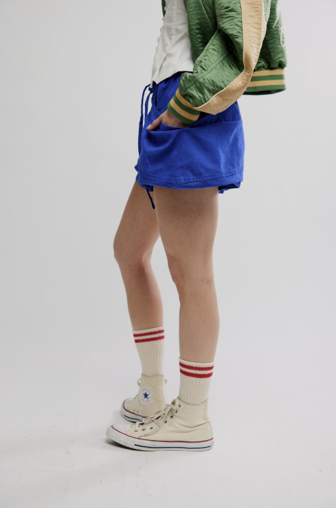 Person wearing blue shorts, a green jacket, and white sneakers with red stripes on a plain background