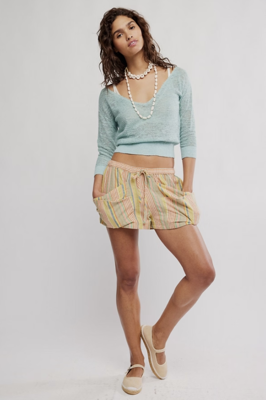 Woman wearing a light blue sweater and striped shorts on a white background
