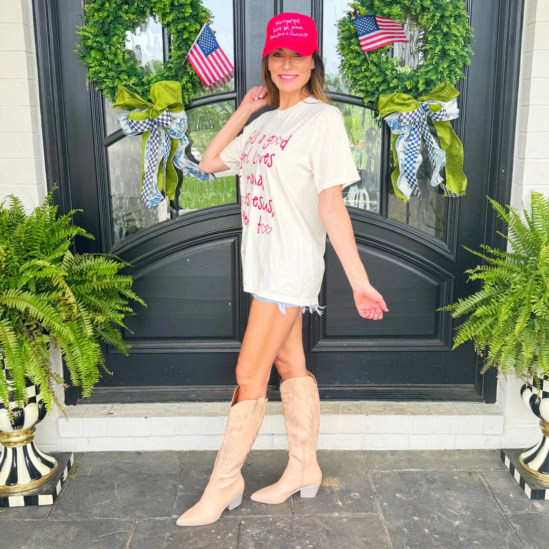 Woman standing in front of a decorated door with wreaths and American flags, wearing a red cap and white t-shirt.
