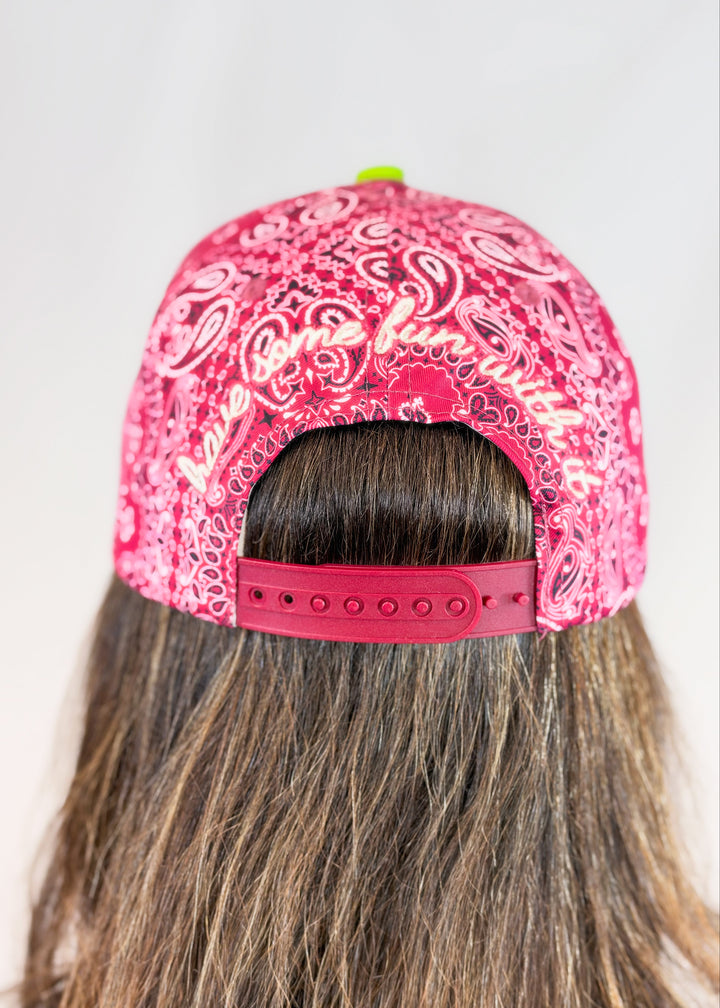 Woman shown from back wearing maroon bandana print trucker hat with &
