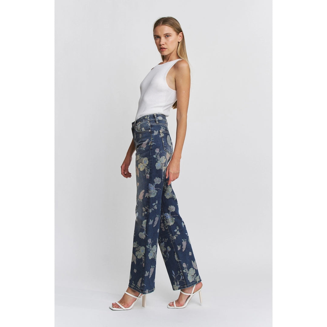 Woman wearing blue floral pants and a white top on a light gray background