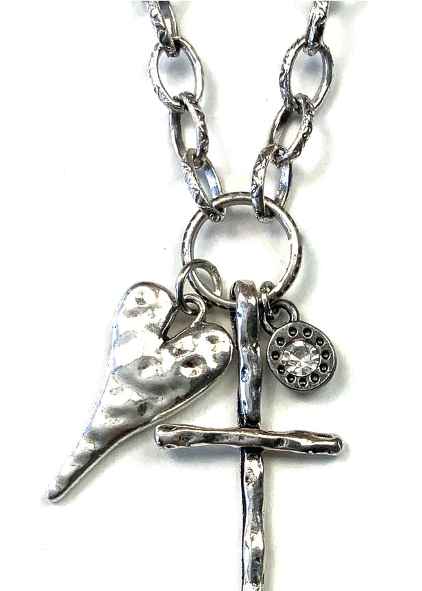 A silver-toned metal necklace featuring a textured cross pendant, a hammered heart charm, and a small round charm, shown on a plain white background.