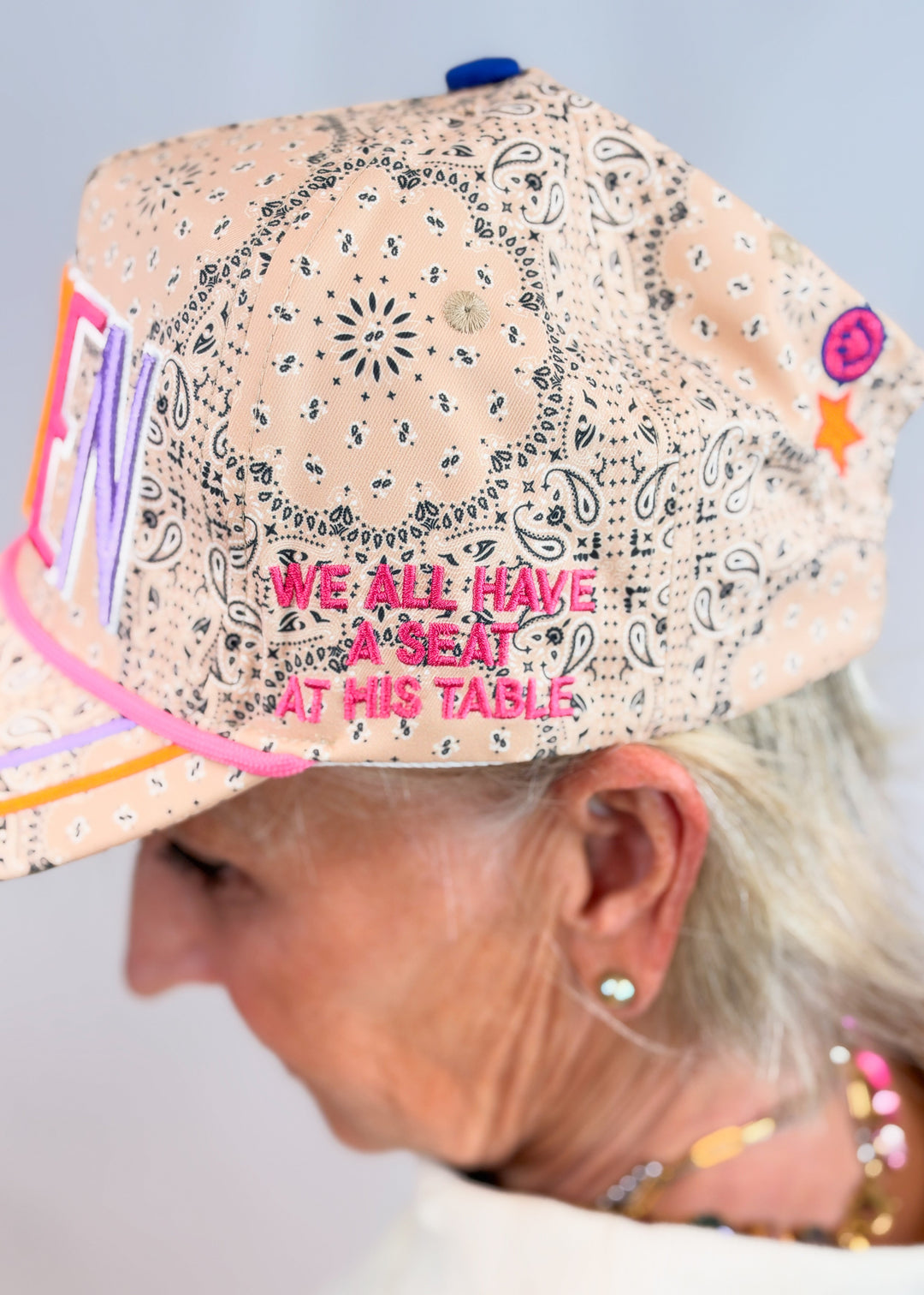 Woman shown from side wearing tan bandana print trucker hate with &