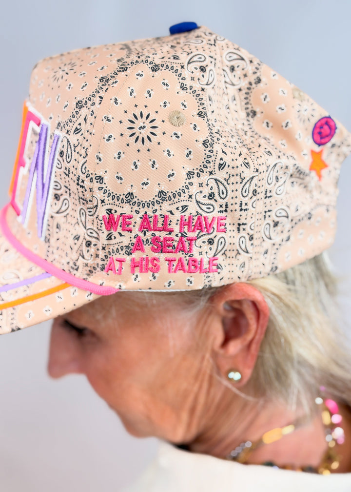 Woman shown from side wearing tan bandana print trucker hate with &