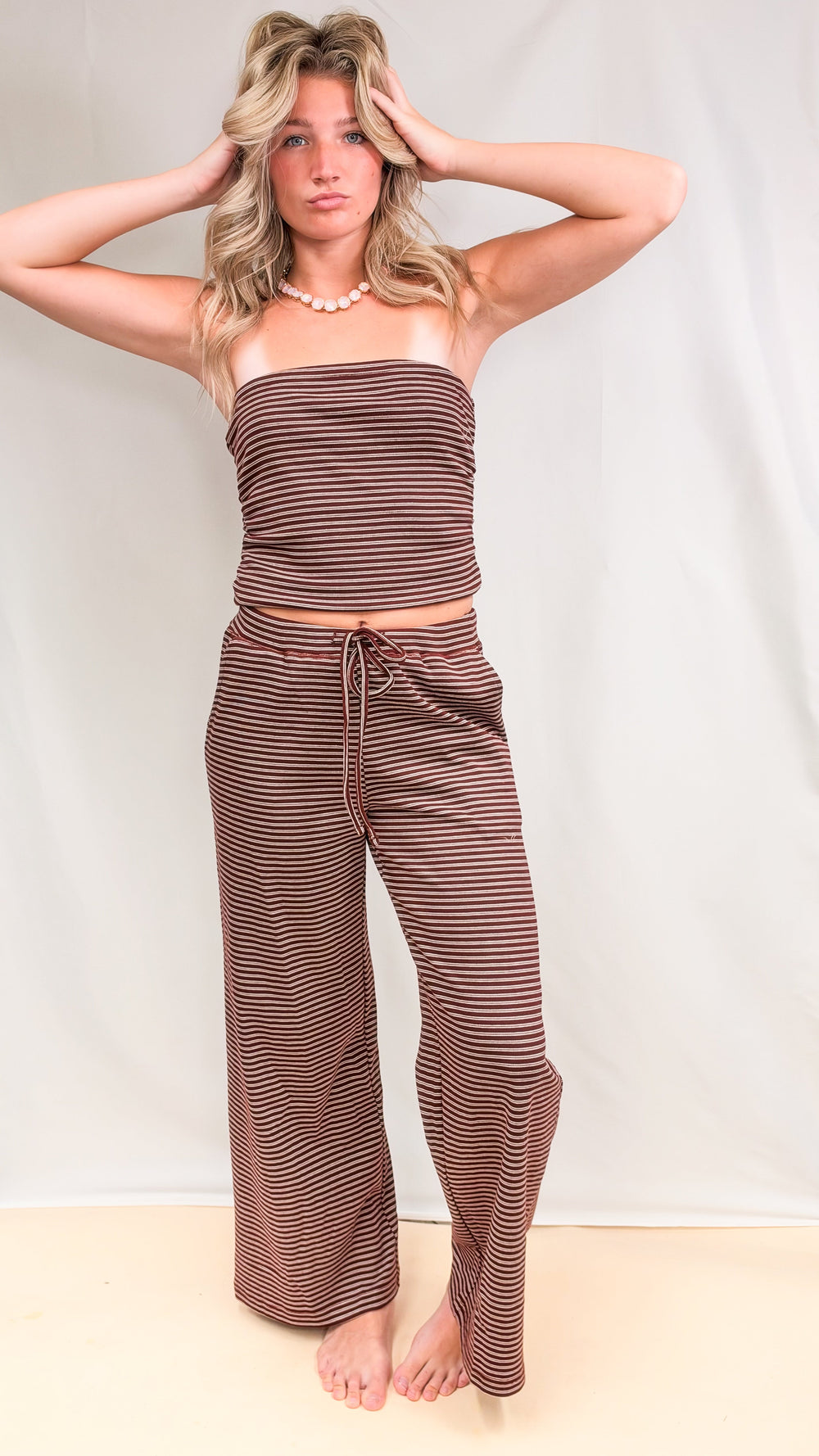 Woman wearing matching burgundy and cream stripe set with tube top and pants on plain background