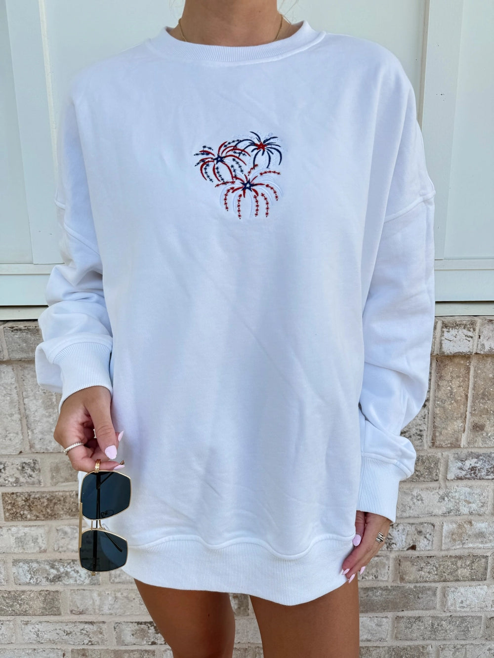 Woman wearing white sweatshirt with fireworks embroidery standing outside