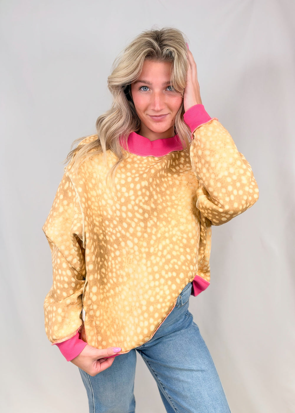 Woman wearing fawn print mock neck sweatshirt with pink ribbed detail on neck and cuffs with jeans on plain background