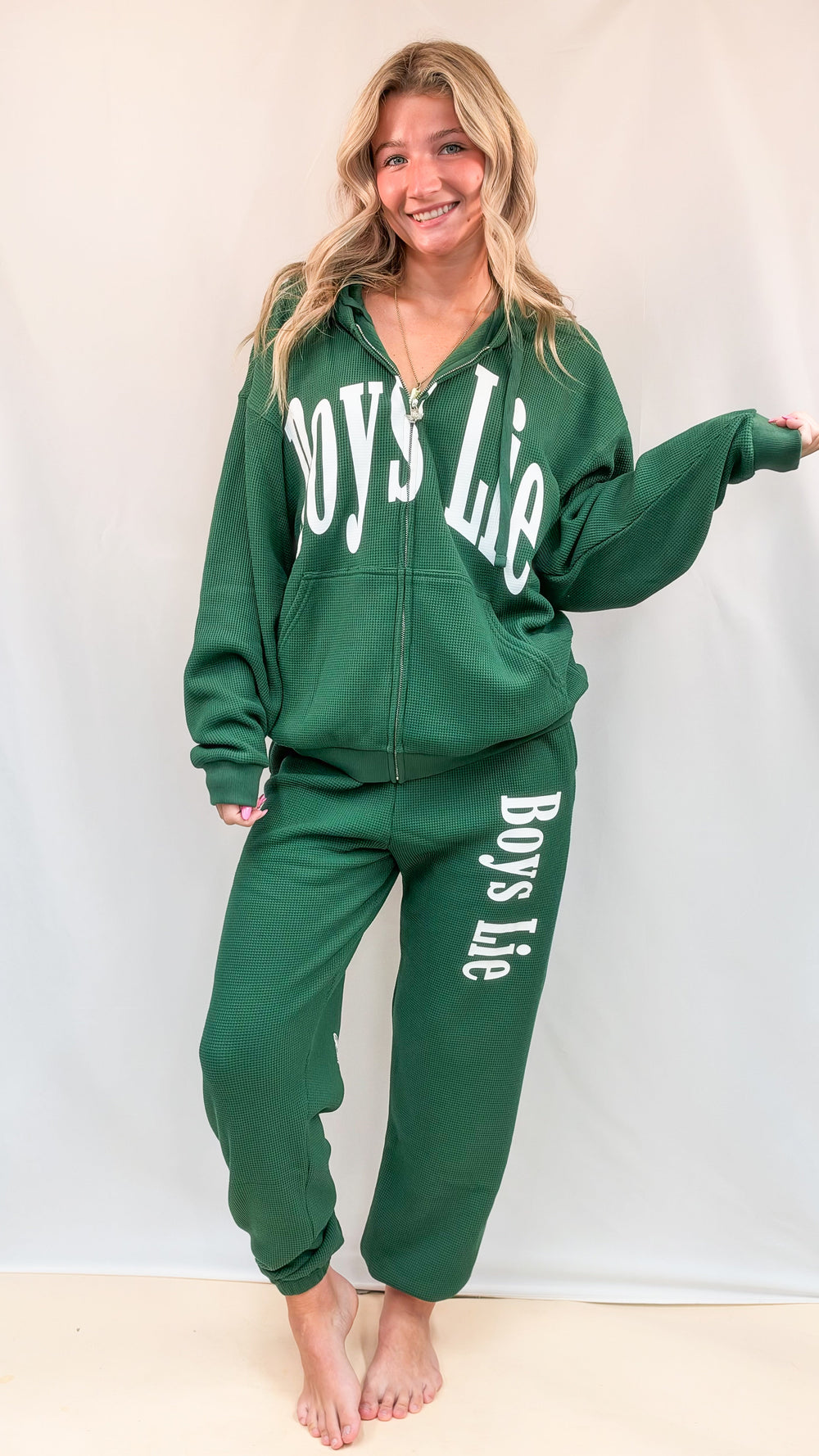 Woman wearing matching green set with 'BOYS LIE' on front and down left leg on plain background