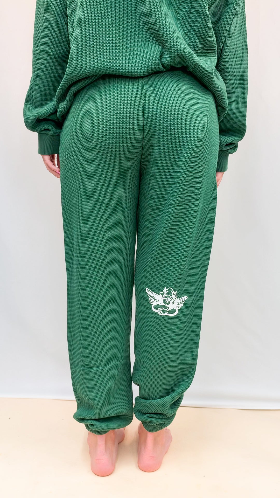 Woman shown from back wearing matching green set with cherub logo on leg on plain background