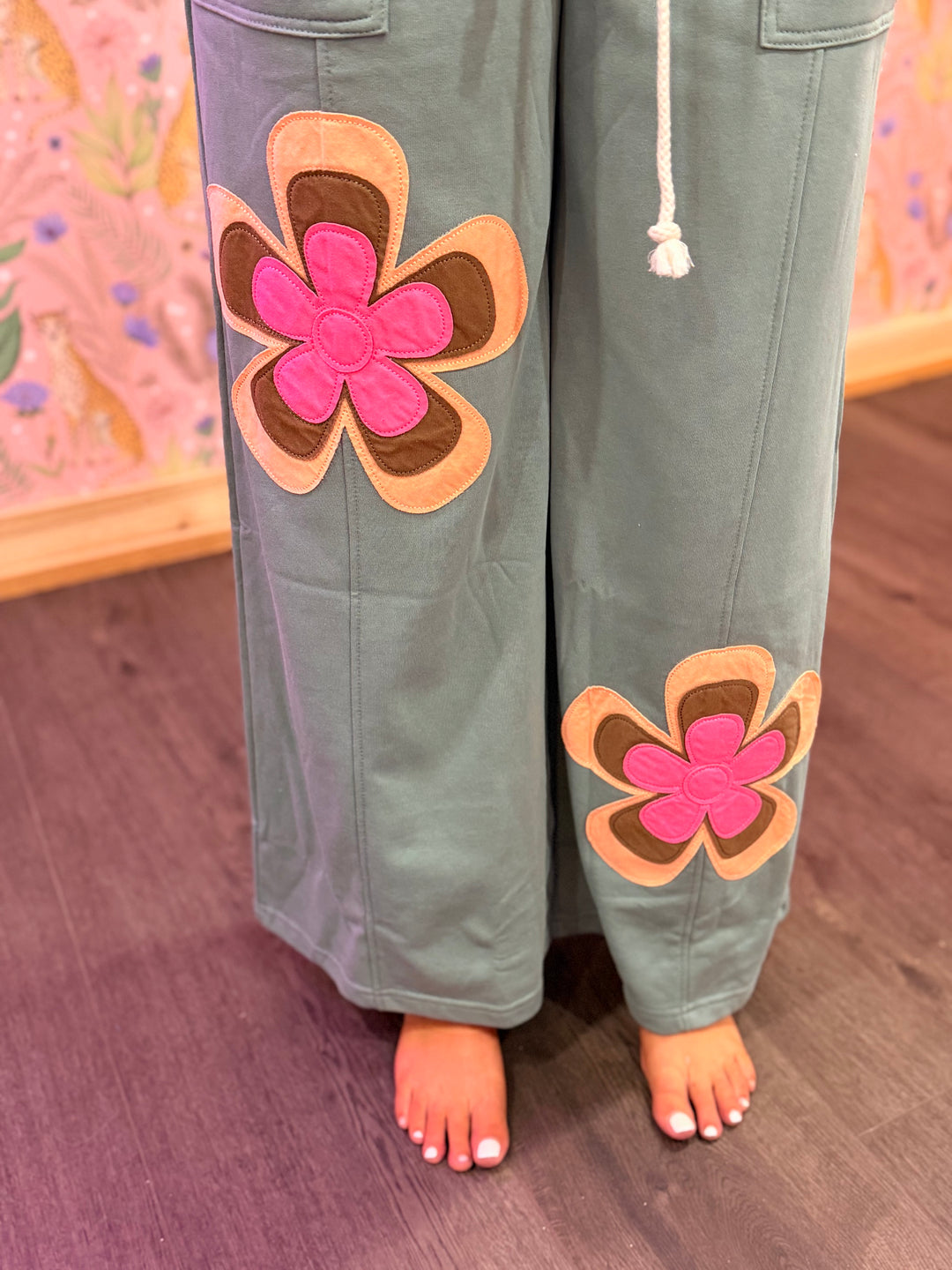 Green pants with pink flower appliqués on a wooden floor.
