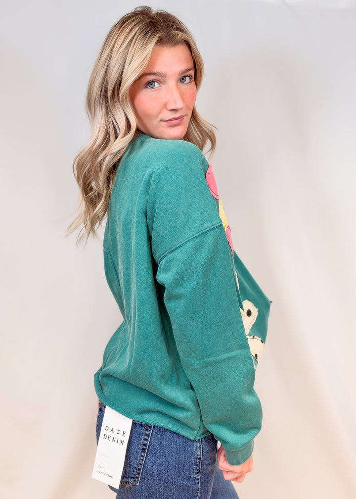 Woman shown from side view wearing teal crewneck with jeans on plain background