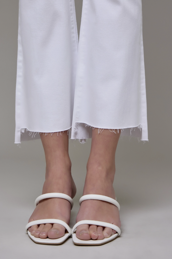 White sandals worn with white pants on a neutral background