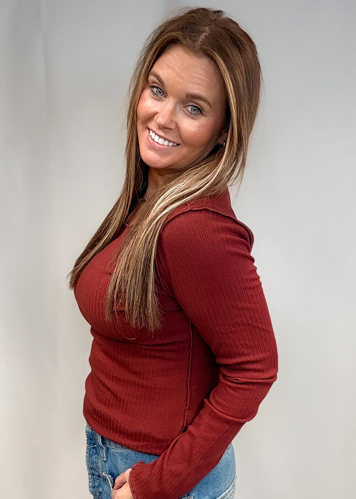 Woman wearing burgundy long sleeve top and jeans on white background