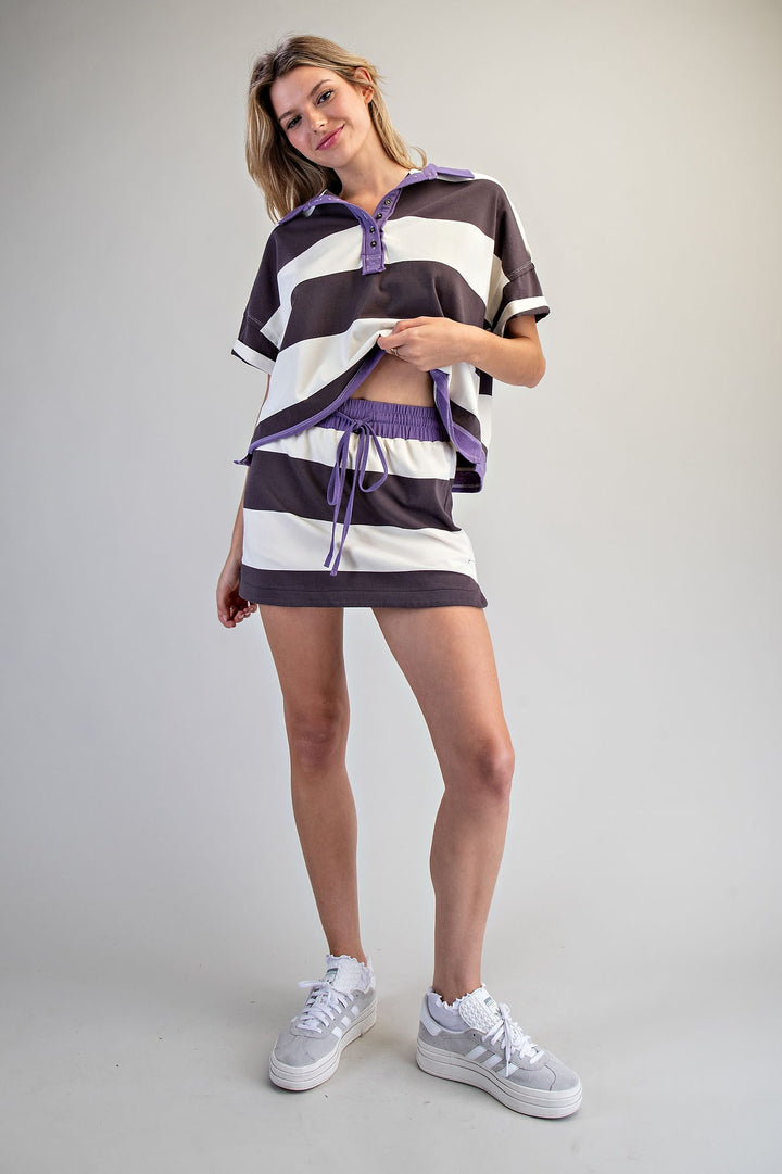 Woman wearing a striped outfit with a brown, white, and purple pattern on a plain background