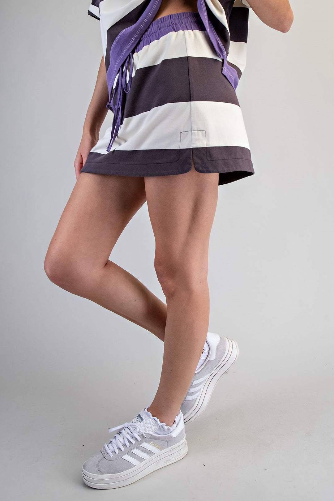 Person wearing a striped shirt, shorts, and white sneakers on a gray background