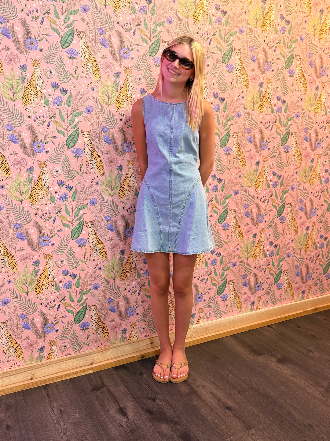Woman in a light blue dress standing in front of a pink wall with animal and floral pattern