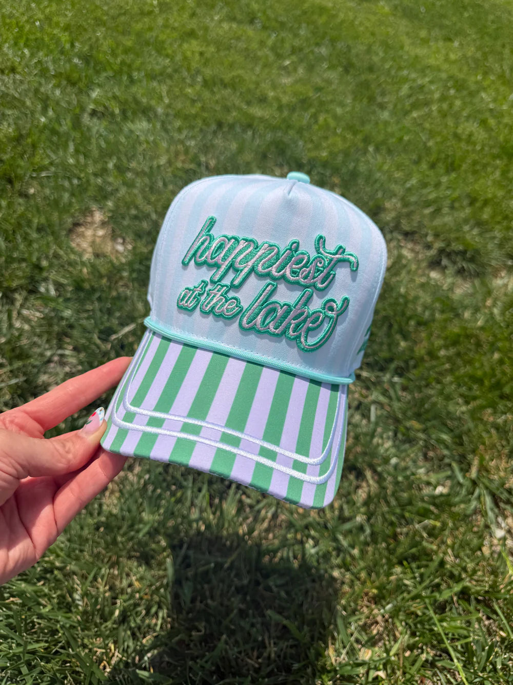 Light blue cap with green text and white stripes held over grass