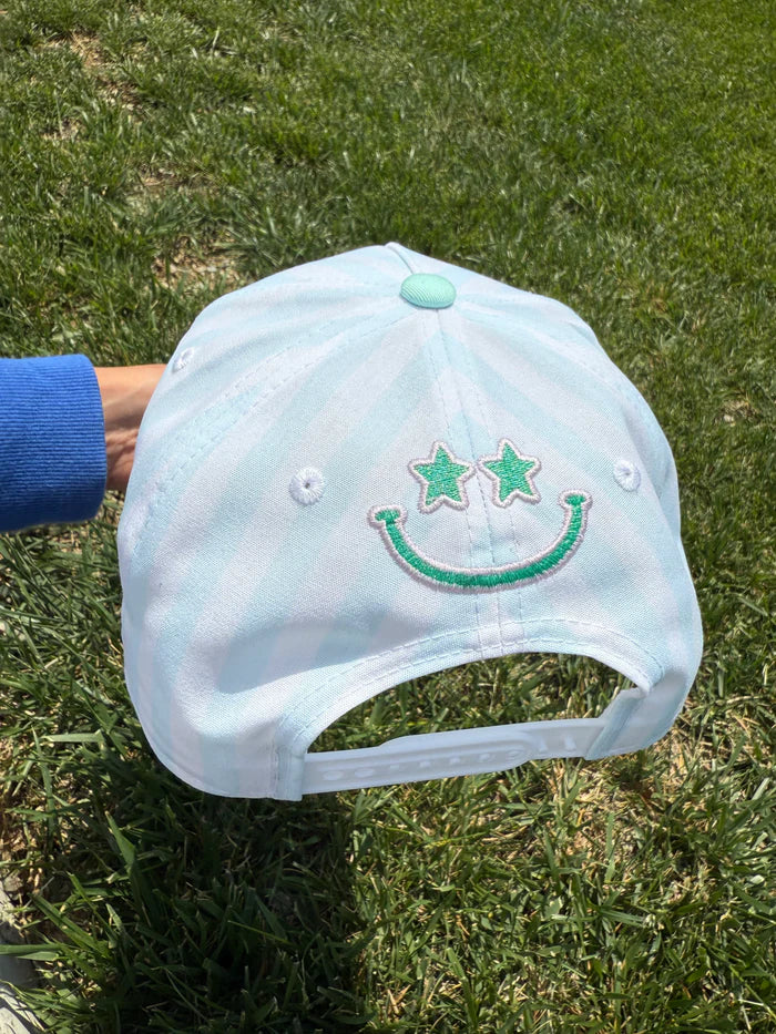 Light blue cap with green smiley face design held on grass