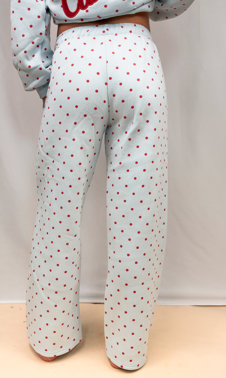 Woman shown from back view wearing blue sweatpants with red polka dots on plain background
