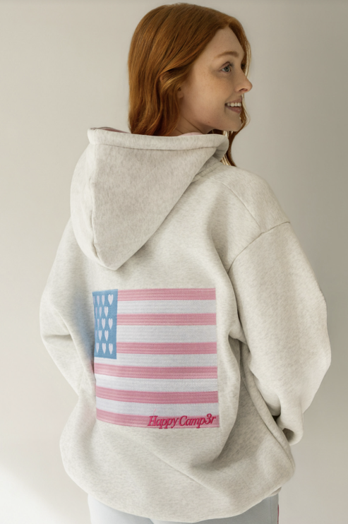 Person wearing a light gray hoodie with an American flag design on the back, on a plain background.