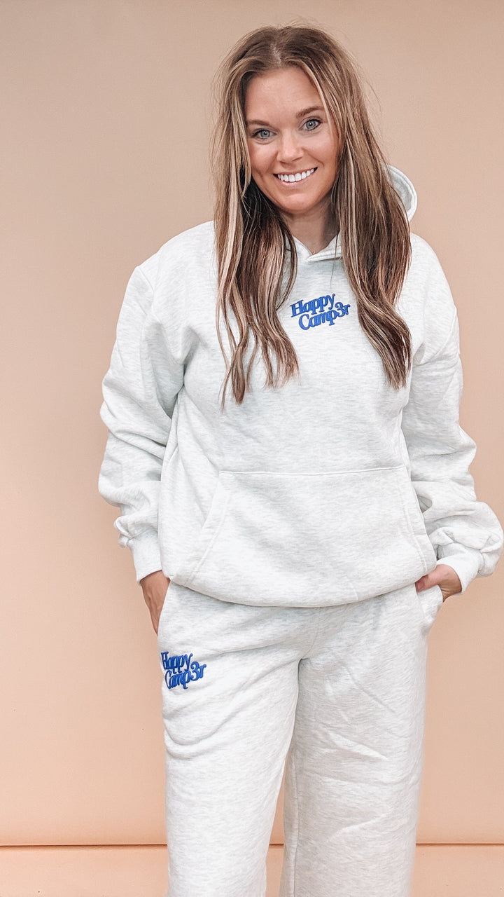 A woman modeling a matching light heather gray sweatshirt and jogger pants set with blue &