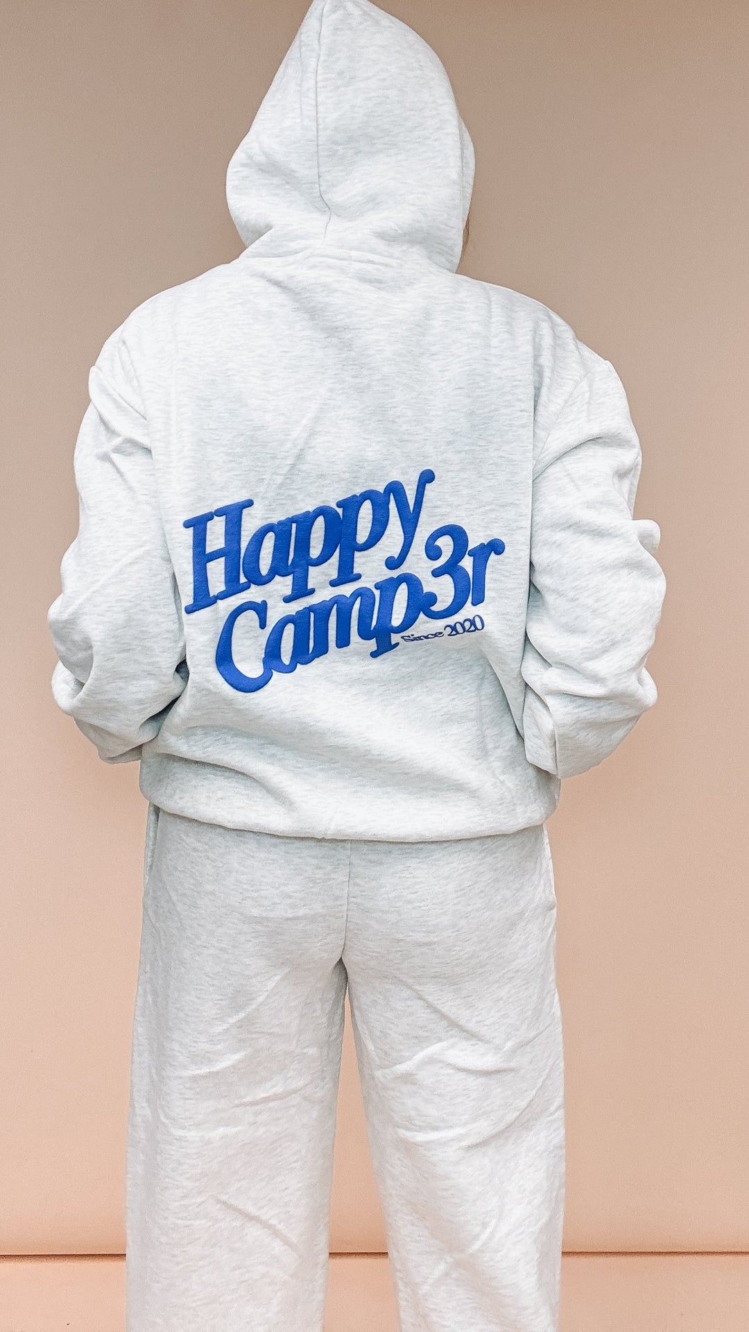 A person shown from the back wearing a light heather gray hoodie and matching sweatpants, with large blue &