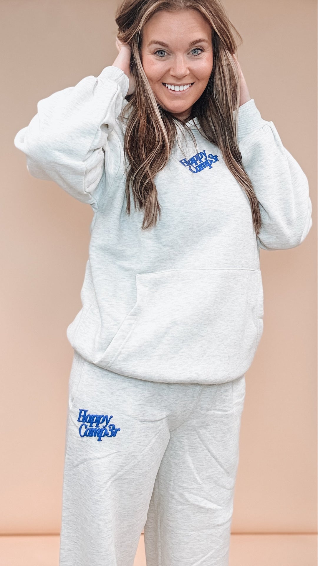 A woman modeling a matching light heather gray sweatshirt and sweatpants set with blue &