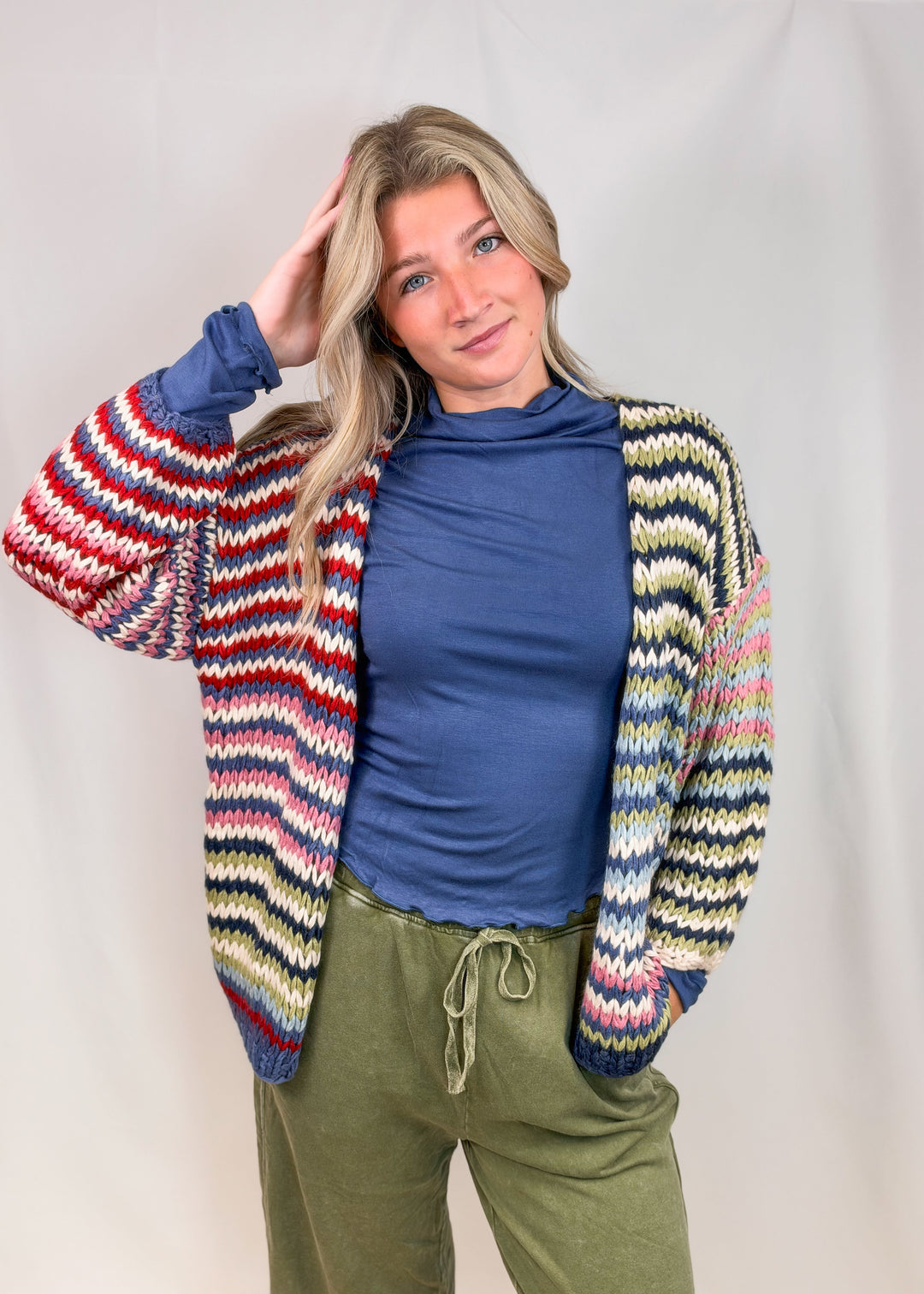 Woman wearing colorful striped cardigan sweater with blue shirt and green pants on plain background