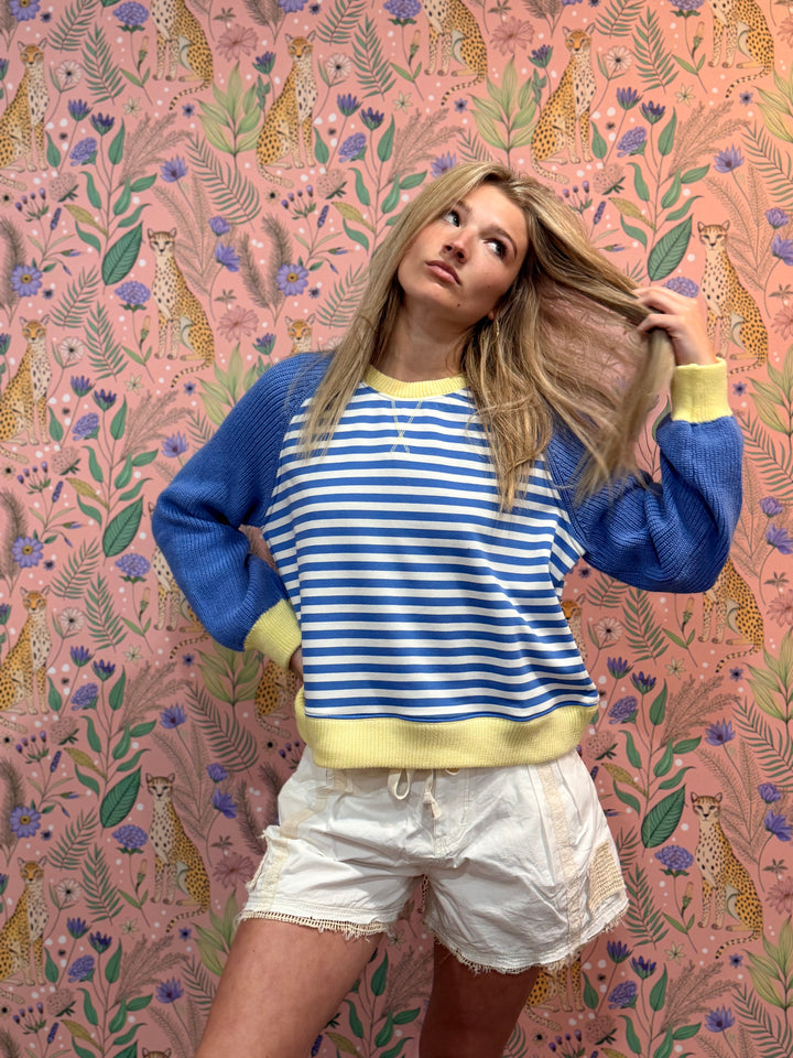 Woman in a striped sweater and shorts standing against a patterned wall with cheetahs and flowers.