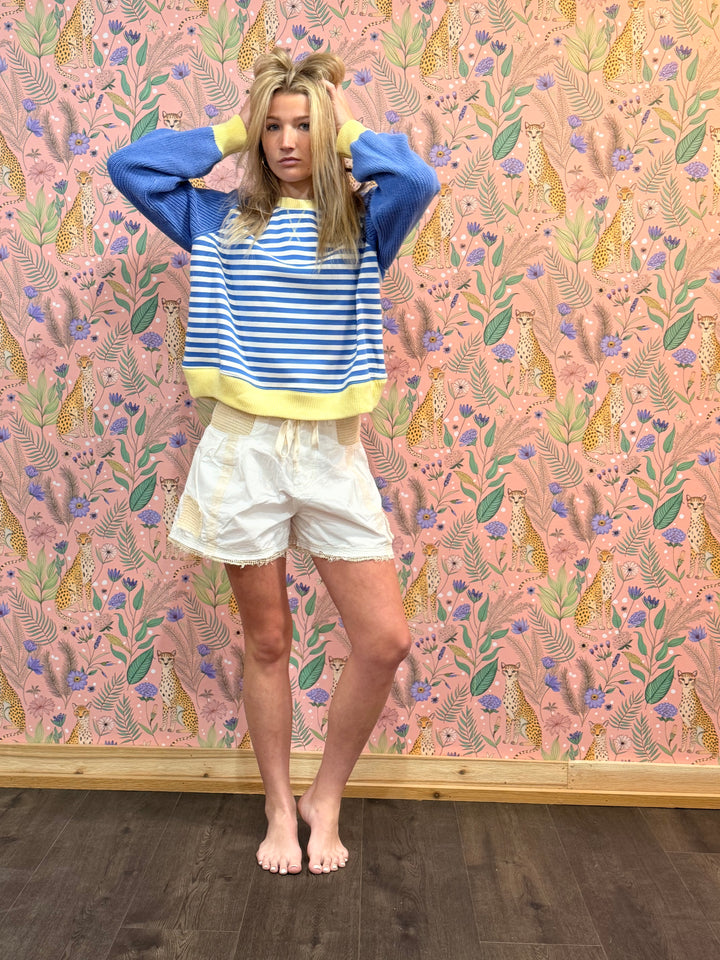 Person wearing a blue and white striped shirt with yellow accents against a patterned wall.