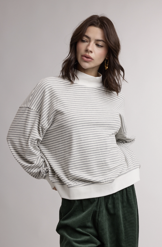 Woman wearing grey and white stripe mock neck sweatshirt on plain background