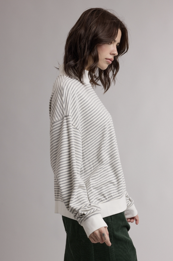 A woman wearing a white long-sleeve knit top with thin gray horizontal stripes, shown in profile against a plain light gray studio background.
