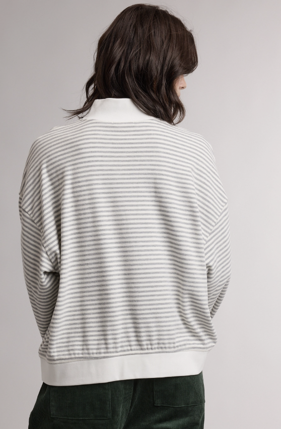 A person shown from the back wearing a light gray and white horizontally striped knit sweater with a white collar, ribbed hem, and cuffs, paired with dark green pants, against a plain light gray studio background.