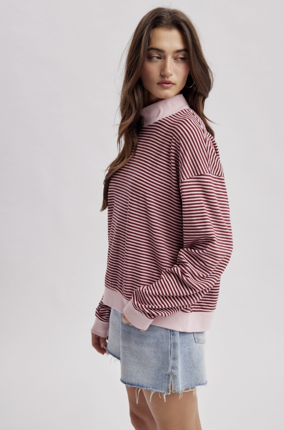 A woman modeling a pink and white striped long-sleeve mock-neck sweatshirt with light blue denim shorts against a light gray studio background.