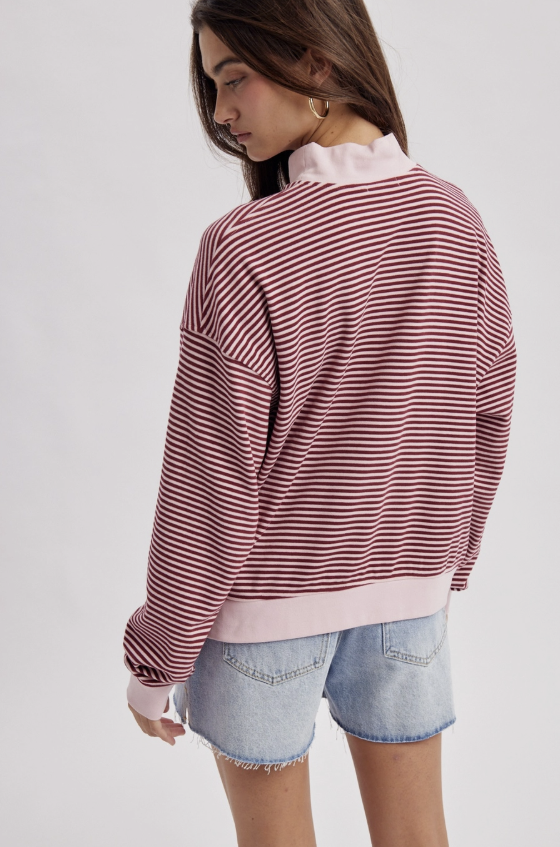 A model wearing a pink and white striped long-sleeve sweatshirt with a light pink mock neck and ribbed hem, paired with denim shorts, shown from a side-back angle against a light gray background.
