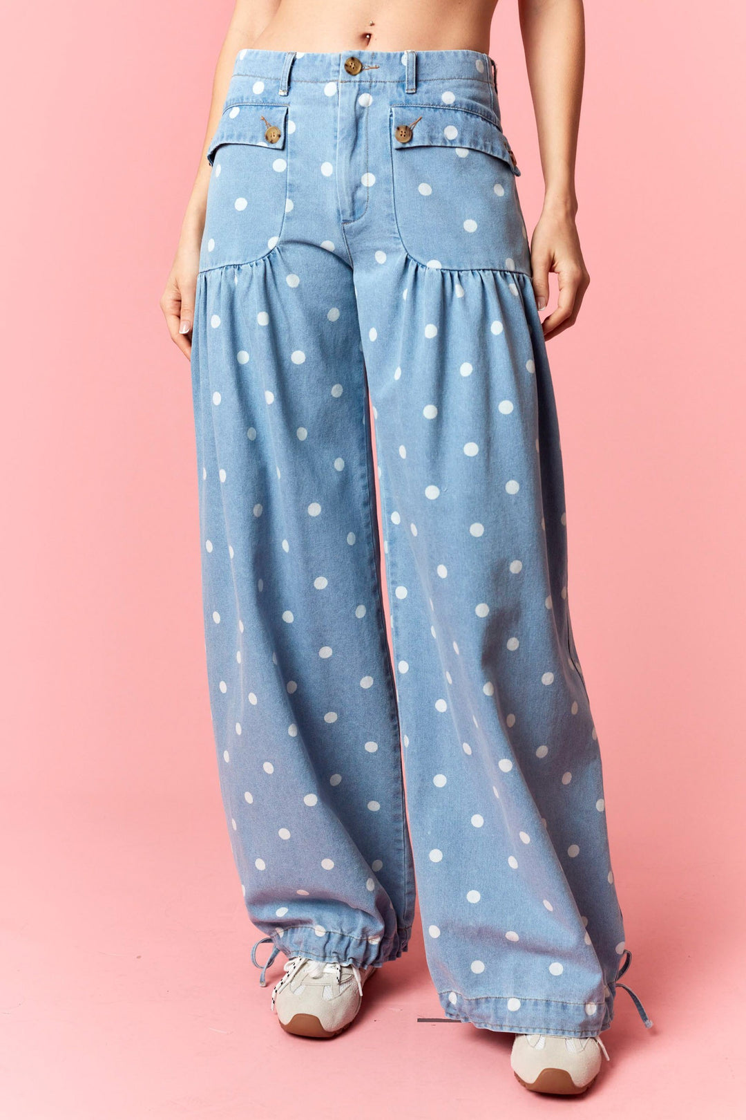 Blue denim pants with white polka dots worn by a person on a pink background
