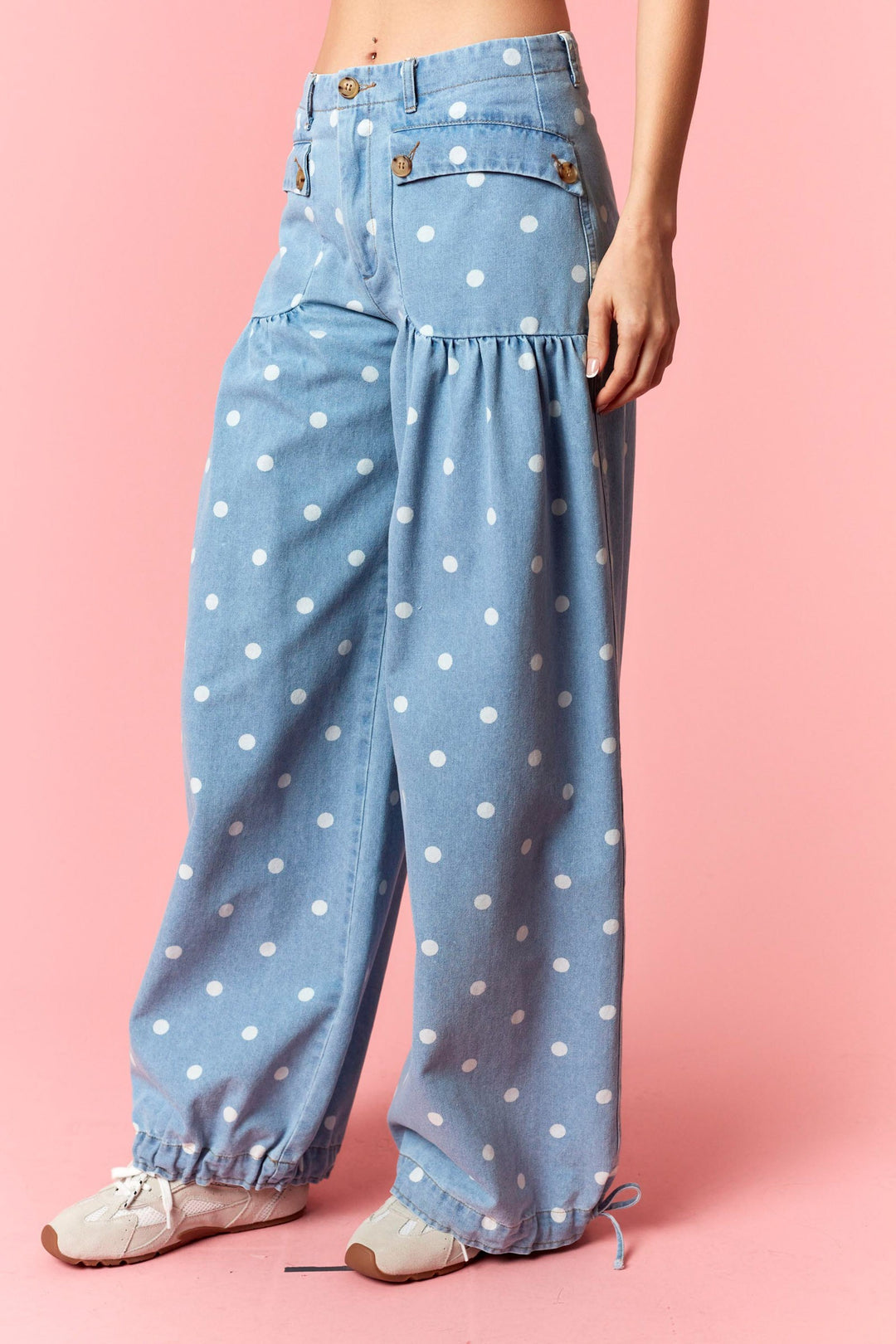 Light blue denim pants with white polka dots worn by a person on a pink background