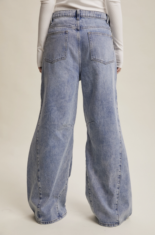 Wide-leg light blue denim jeans shown from the back on a model, featuring a faded wash and classic pocket design, against a solid light beige background.