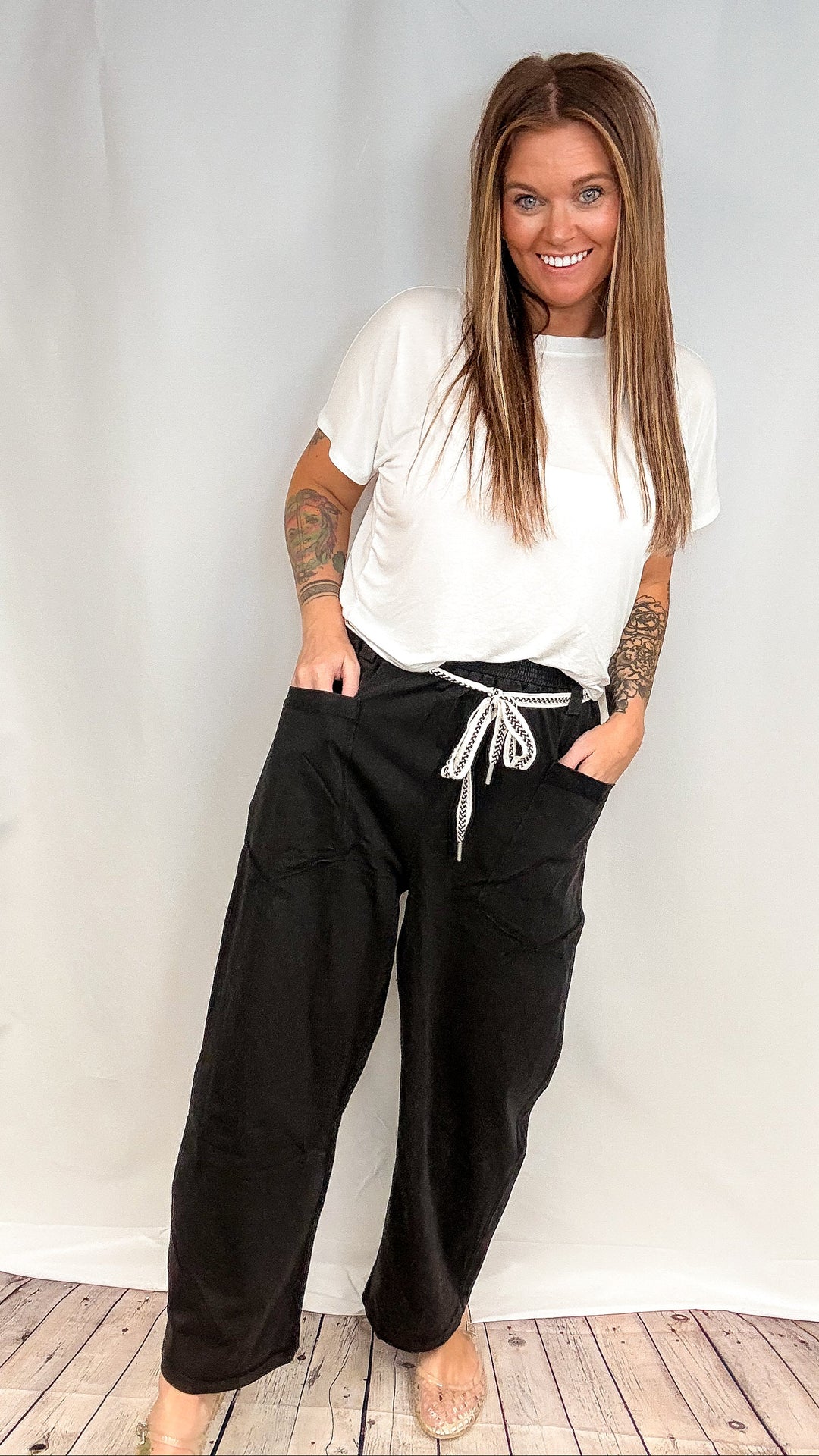 Woman wearing white short sleeve top and black barrel sweatpants on white background