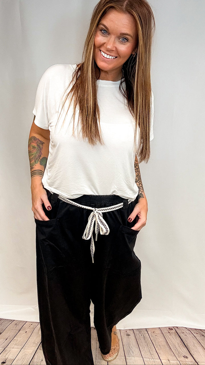 Woman wearing white short sleeve shirt and black barrel sweatpants on white background