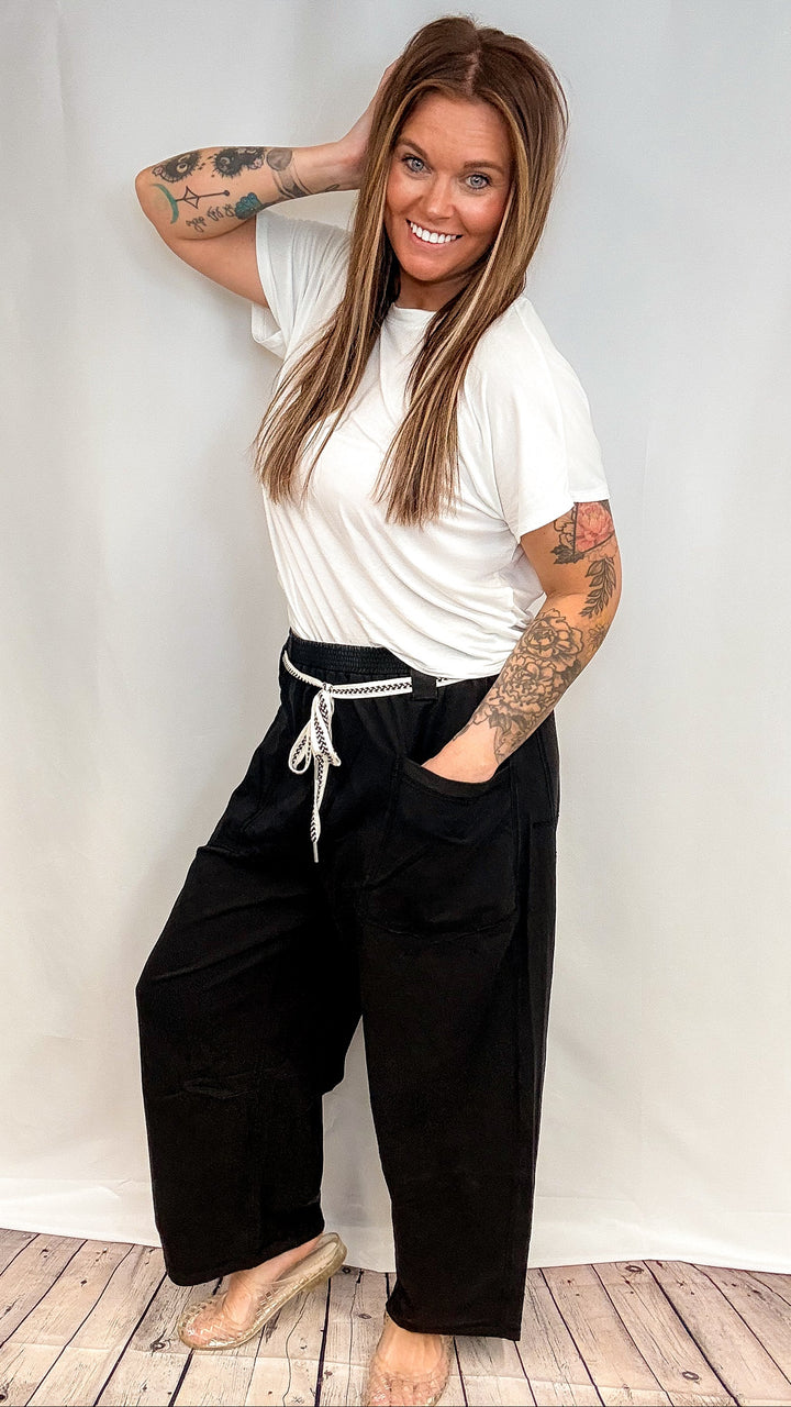 Woman wearing white short sleeve shirt and black barrel sweatpants on white background