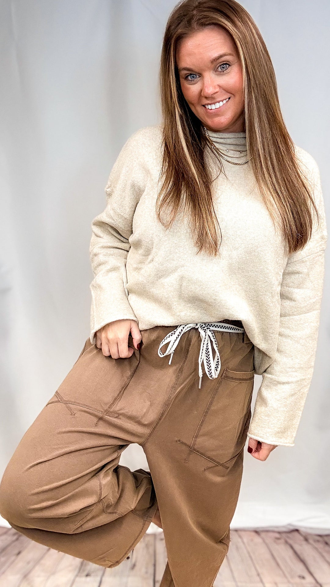 Woman wearing beige top and brown pants on plain background