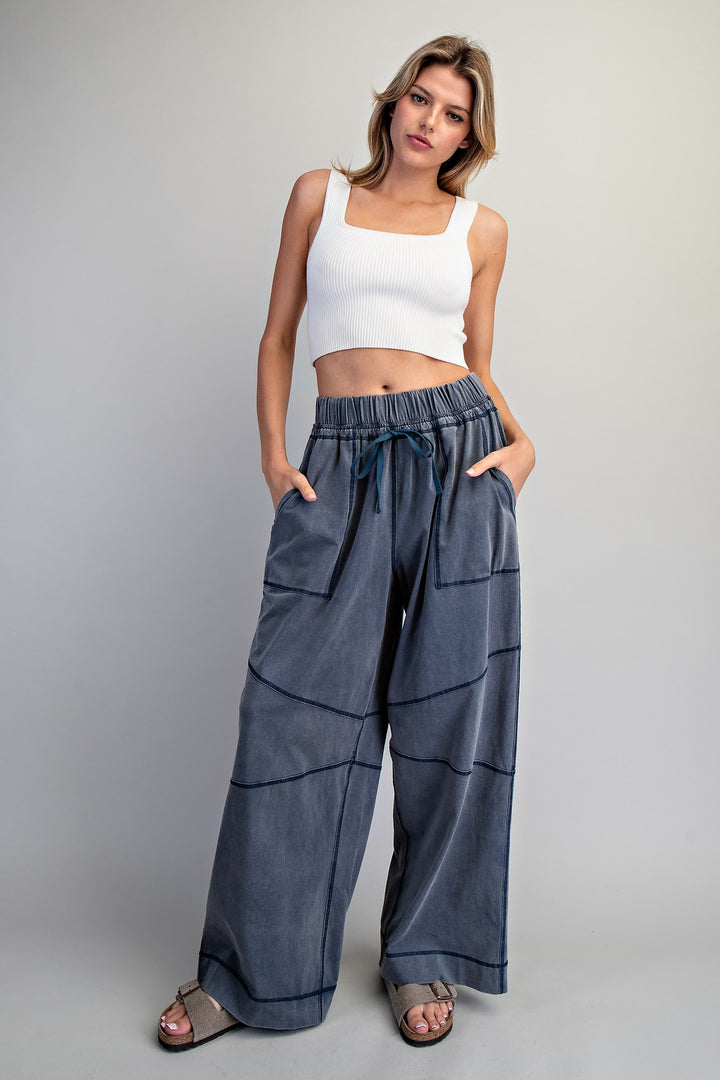 Woman wearing a white top and blue wide-leg pants on a gray background