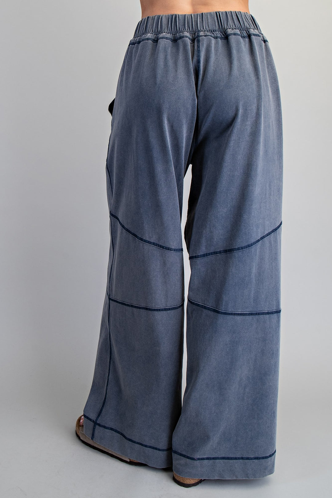 Wide-leg pants in a washed slate blue fabric, shown from the back on a model. The pants feature horizontal contrast stitching and an elastic waistband.