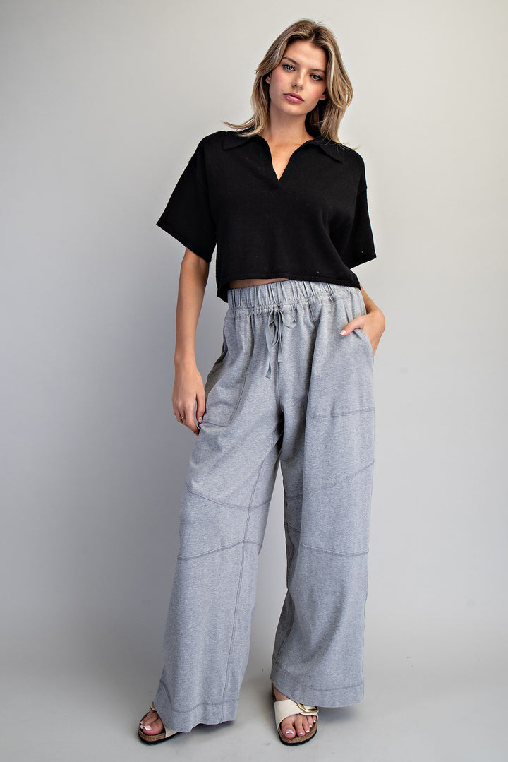 A woman modeling a black short-sleeve polo crop top and light gray wide-leg drawstring pants against a plain light gray studio background.
