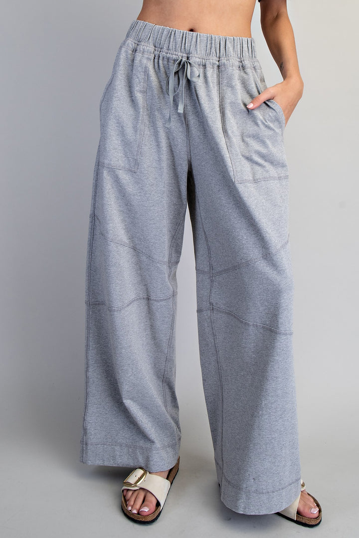 A person wearing light heather gray wide-leg drawstring pants with side pockets, paired with white slide sandals, shown against a plain light gray studio background.