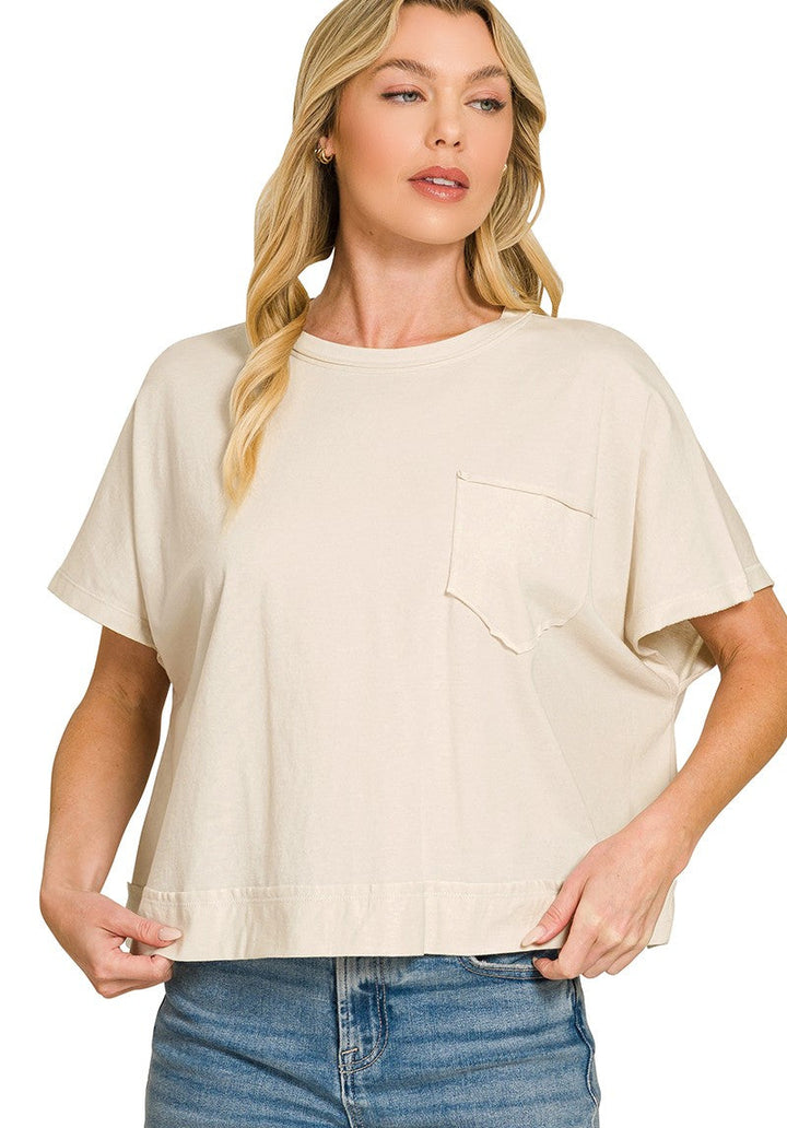 A woman wearing a cream-colored short-sleeve t-shirt with a chest pocket, paired with blue jeans, against a plain white background.